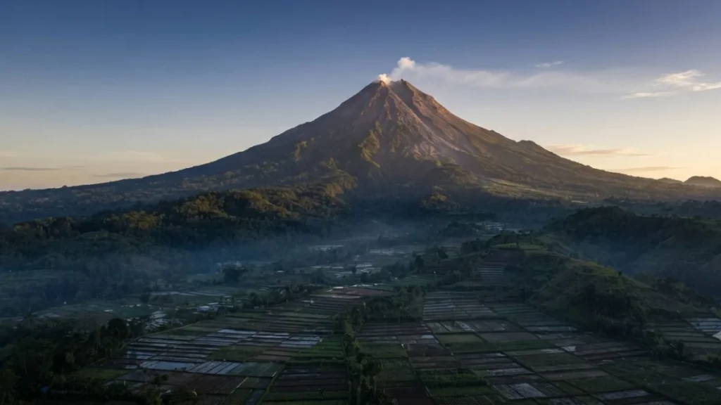 Mount Merapi Yogyakarta volcanic cone at dawn with smoke plume above highland Java landscape