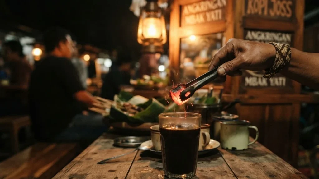 Glowing charcoal dropped into a glass of kopi joss at a Yogyakarta angkringan